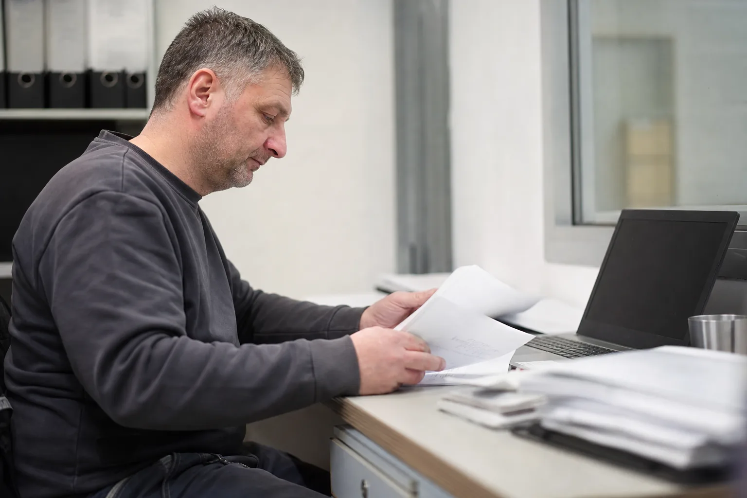 Elektrotechniker ordnet Rechnungsunterlagen am Schreibtisch
