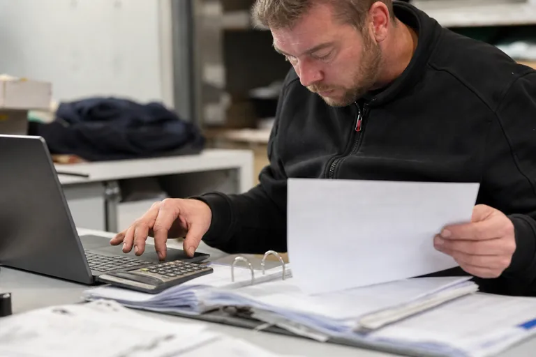 Arbeitsplatz im Handwerksbetrieb mit Laptop, Rechnungsordner und Arbeitszetteln